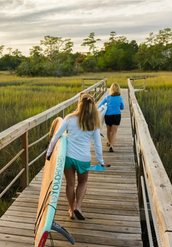 Paddleboarders crossing a marsh boardwalk near Channel Haven
